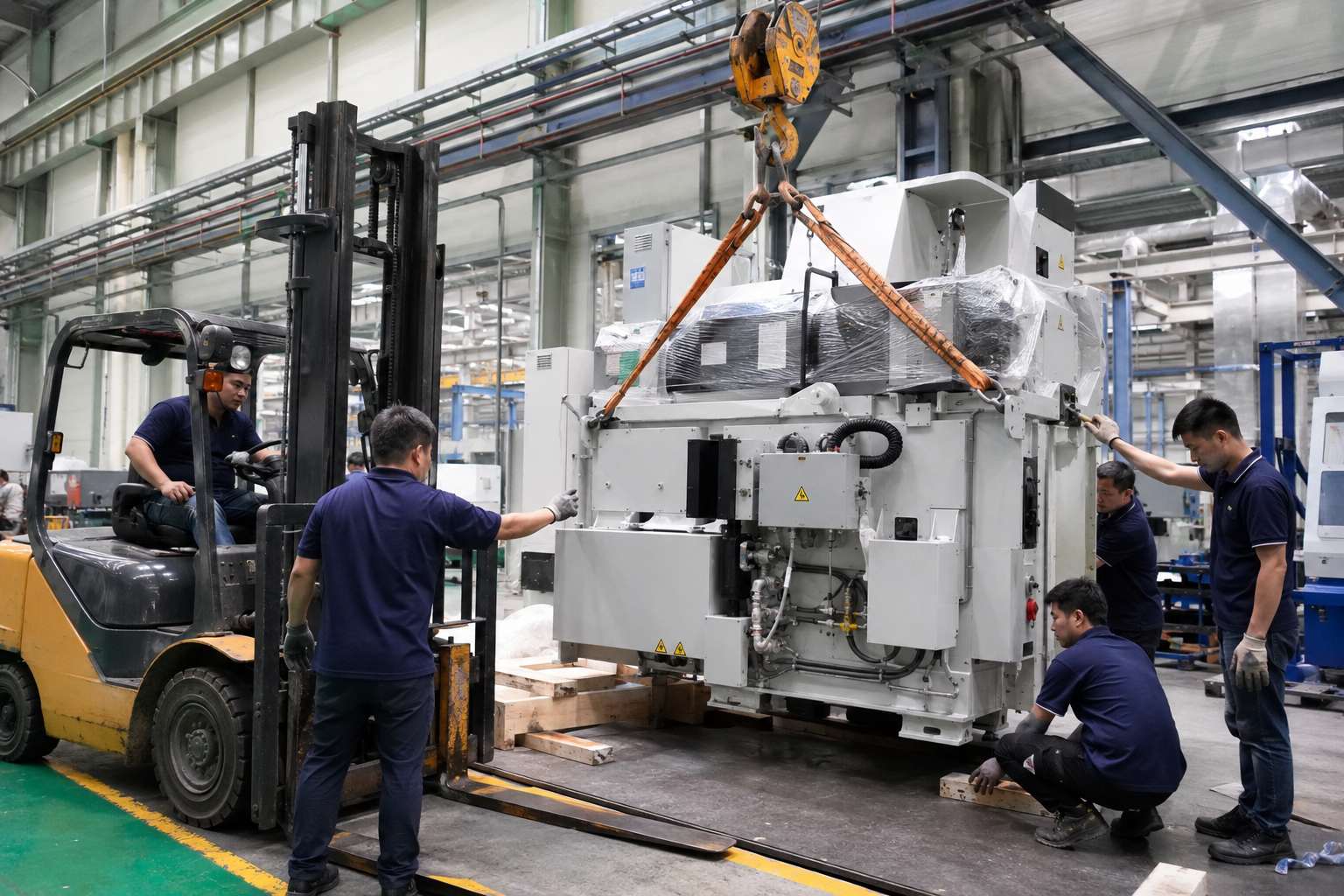 Workers positioning heavy machinery with forklift and crane during industrial equipment installation